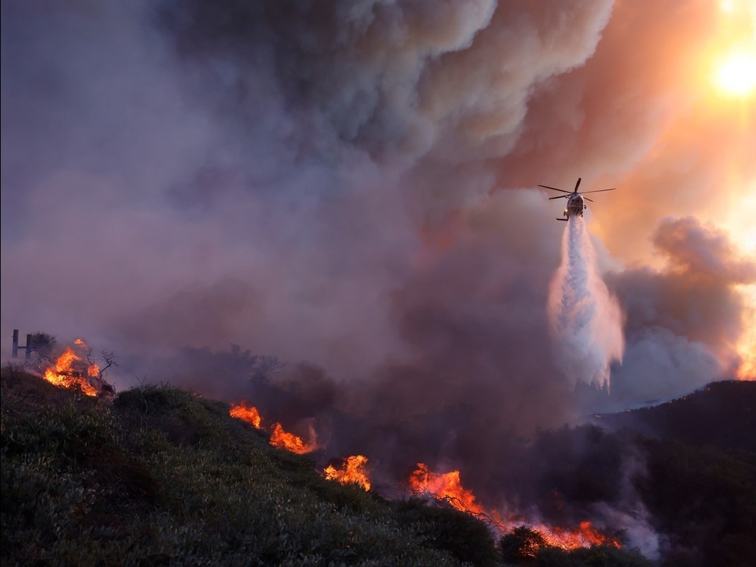A helicopter drops water on the advancing Palisades fire in Los Angeles.